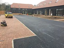 Tarmac surfacing to a shared courtyard with a roller and block paved parking bays