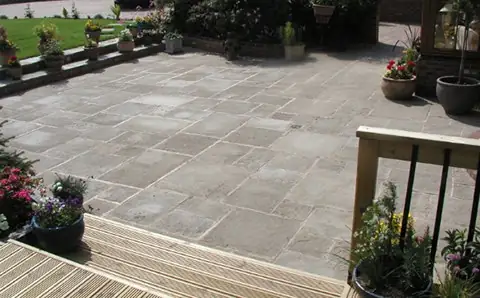 Grey paving slab patio next to timber decking with potted plants
