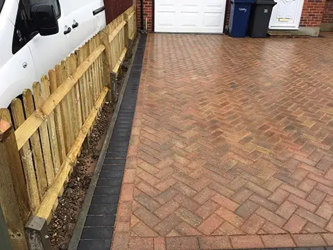 Herringbone block paved driveway running alongside a new timber fence