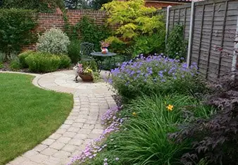 Landscaped garden with a curved paved path, lawn and colourful planting beside a fence