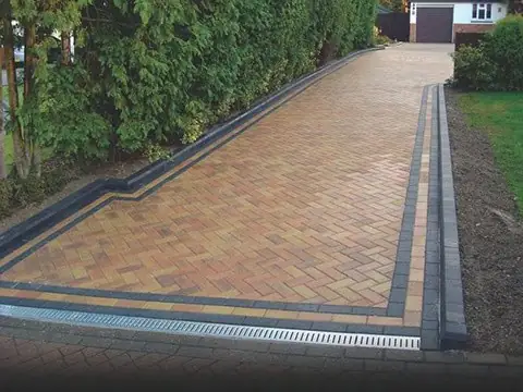 Long herringbone block paved driveway with a charcoal border and a drainage channel