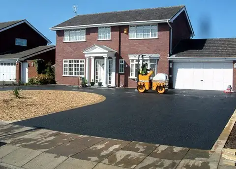 Freshly laid tarmac driveway in front of a detached brick house with a roller on site
