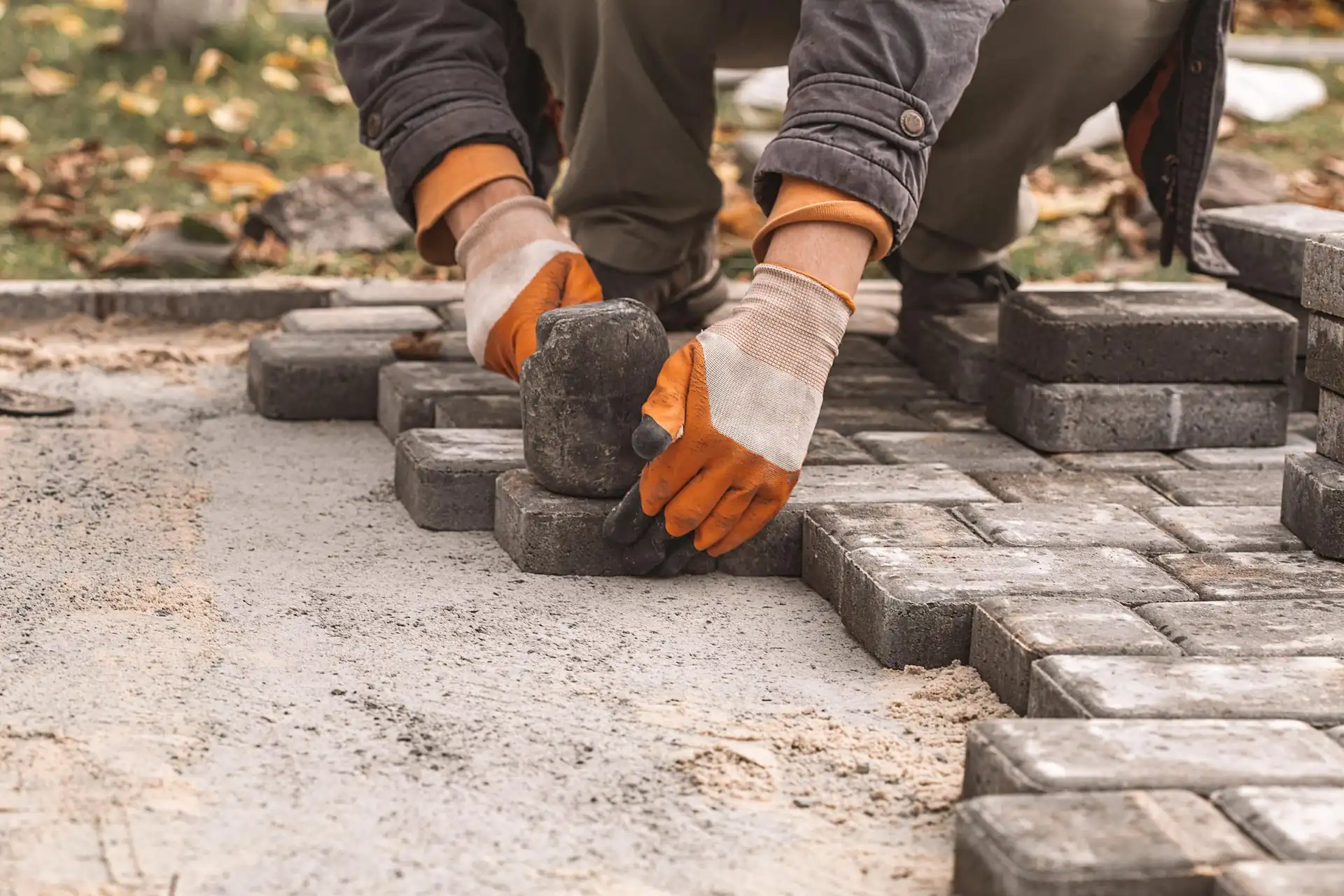 Paver in work gloves laying concrete paving blocks on a sand bed